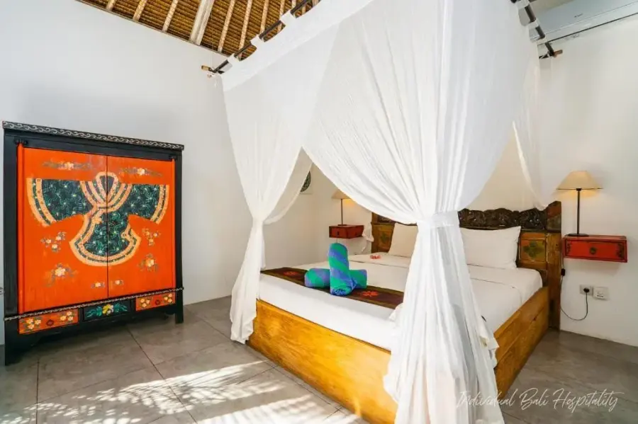 A canopy bed under white netting, a painted Javanese panel above the headboard