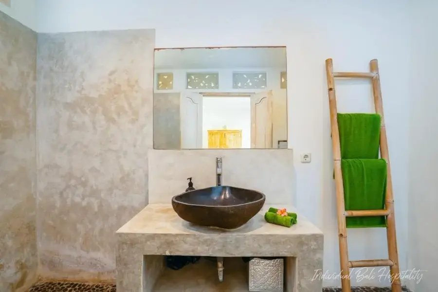 A river-stone bathroom — carved basin, ladder of green towels, morning light