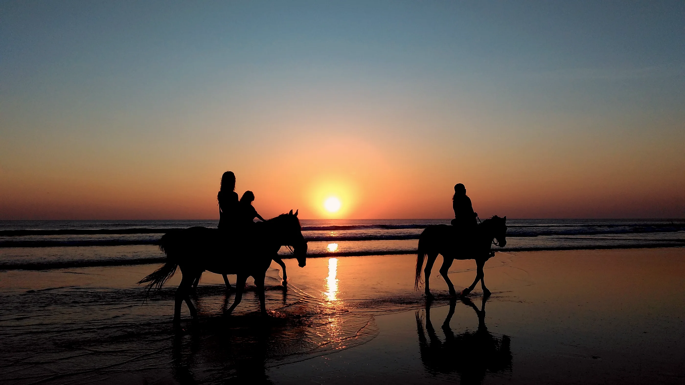 Cavaliers le long de la plage au coucher du soleil