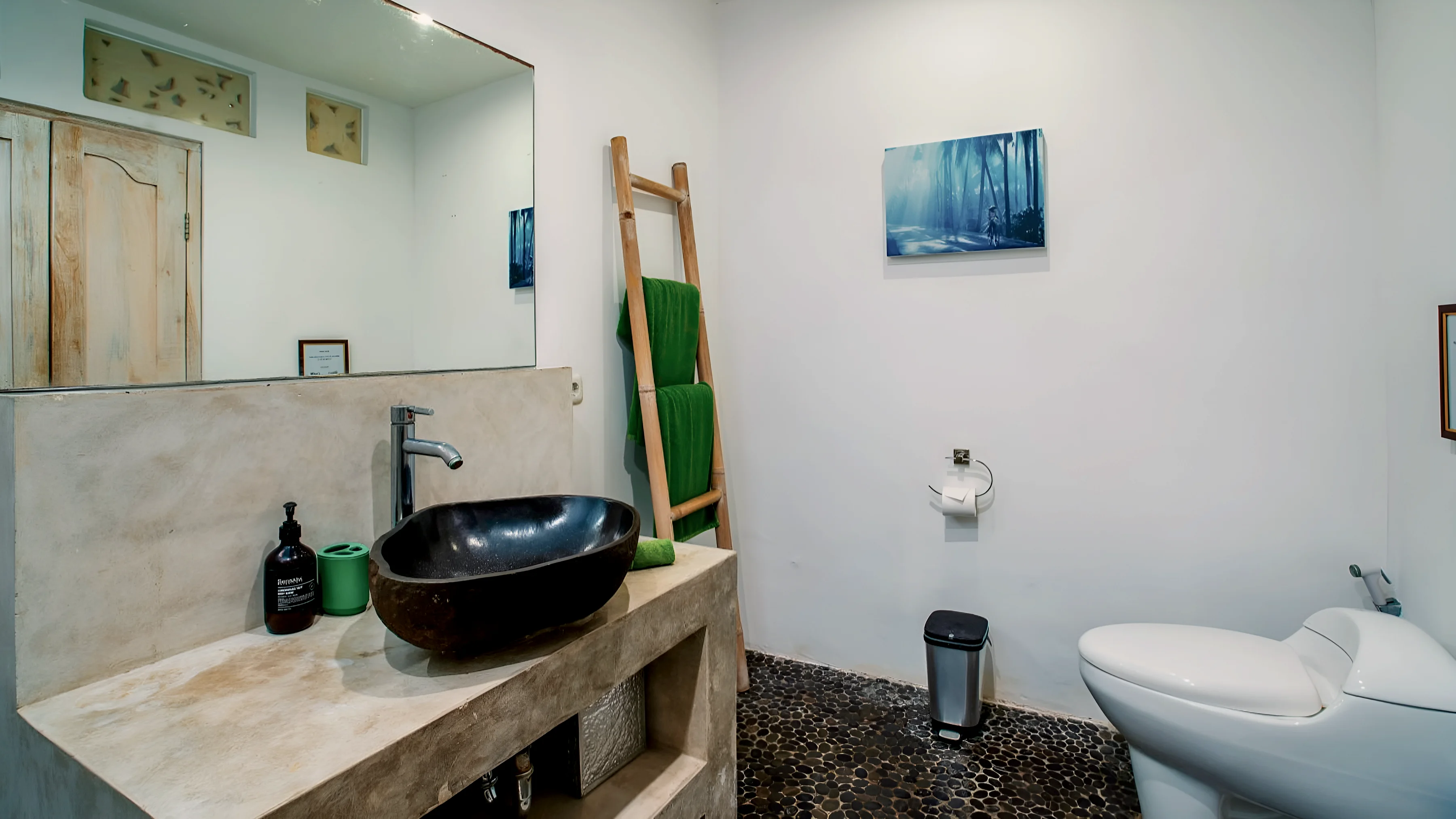Kamar mandi dengan wastafel batu, lantai kerikil, dan tangga handuk