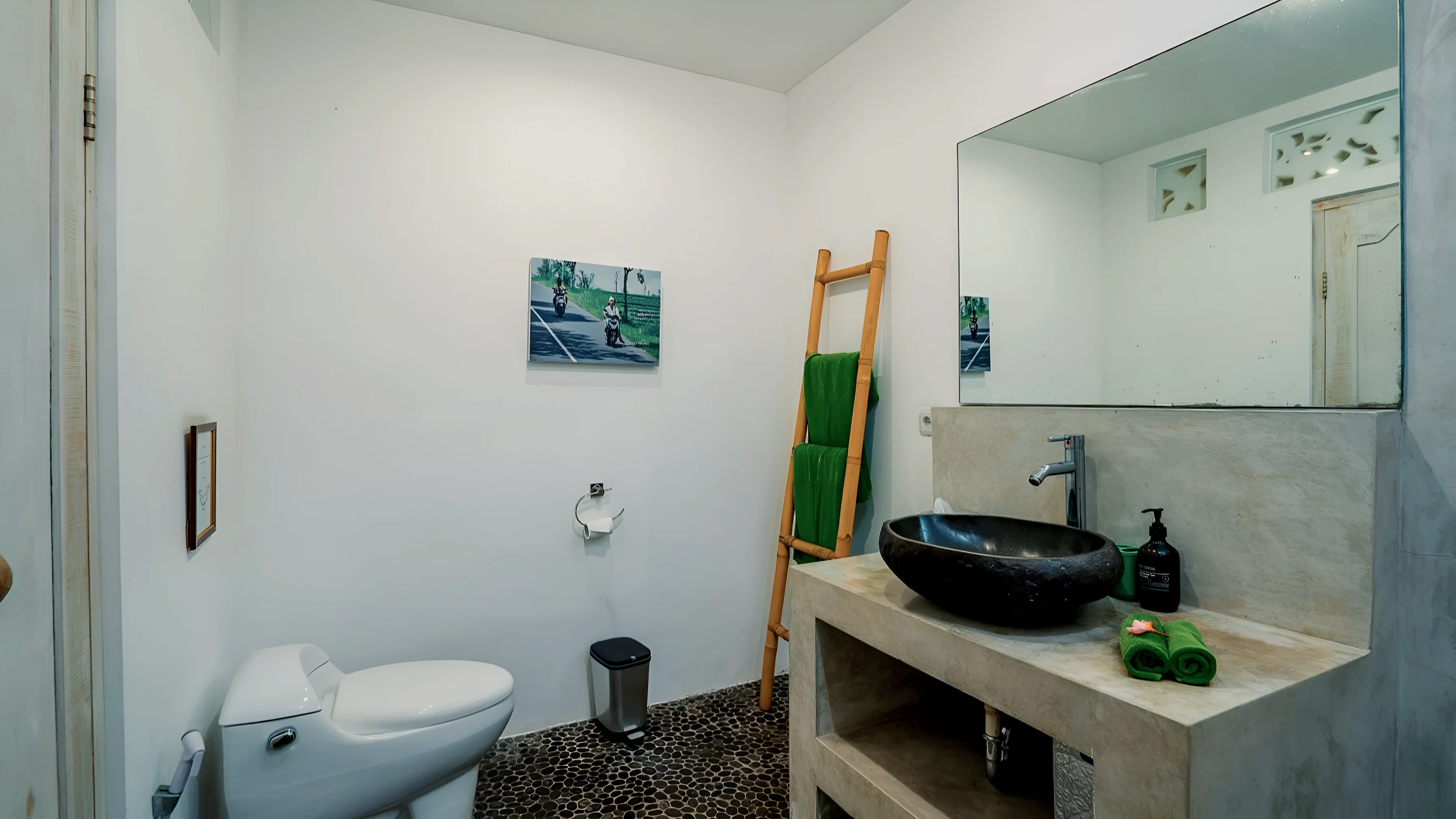 Kamar mandi dengan wastafel batu, cermin, dan tangga handuk