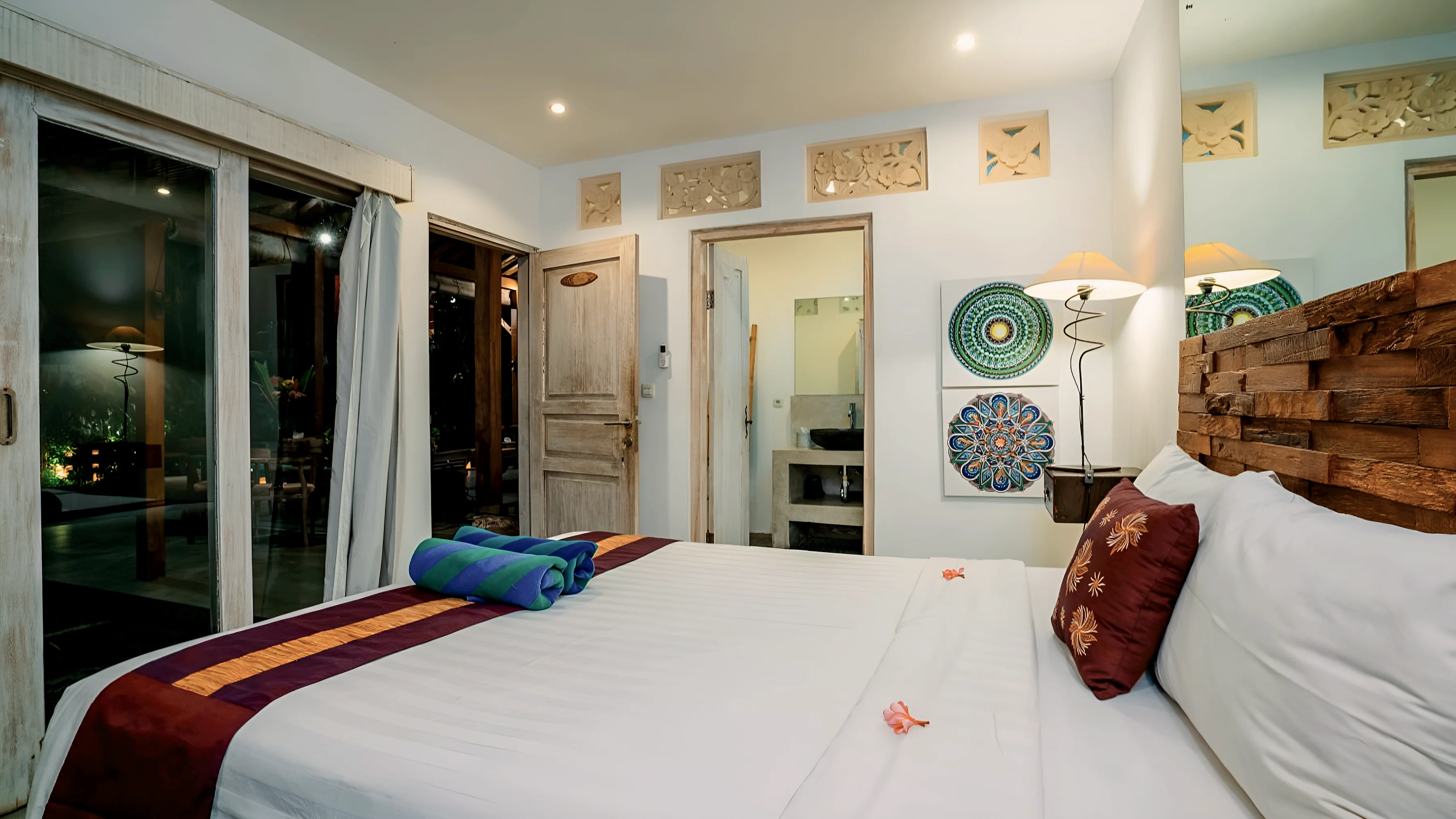 Kamar tidur dengan kepala ranjang kayu berukir dan pintu terbuka ke kamar mandi