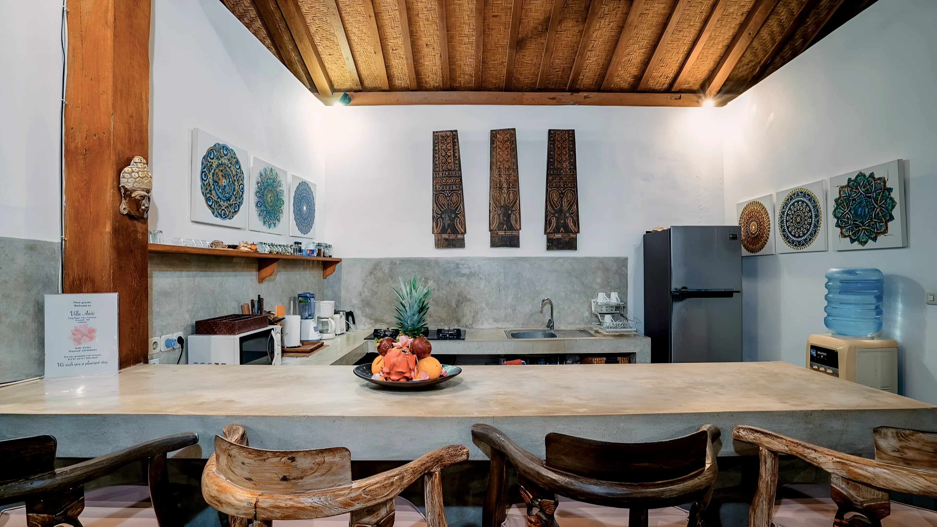 Bar dapur dengan kursi tinggi, mangkuk buah, dan panel ukir di dinding